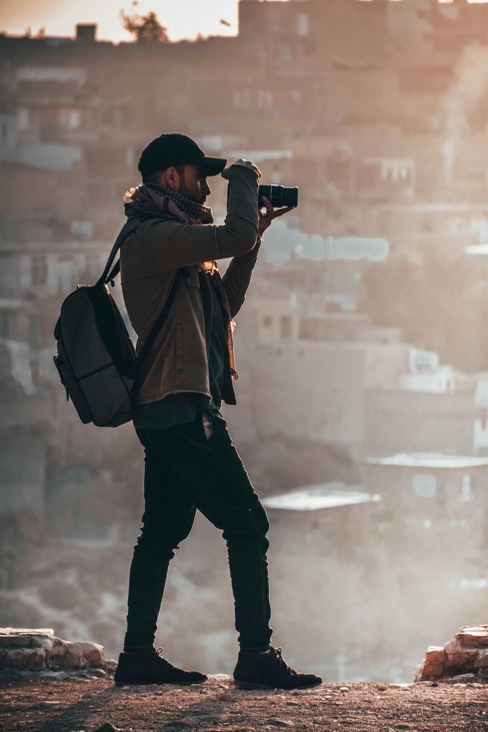 A photographer in a jacket capturing a city view with a DSLR during sunset.